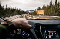 a car driving down a road with a cabin in the background